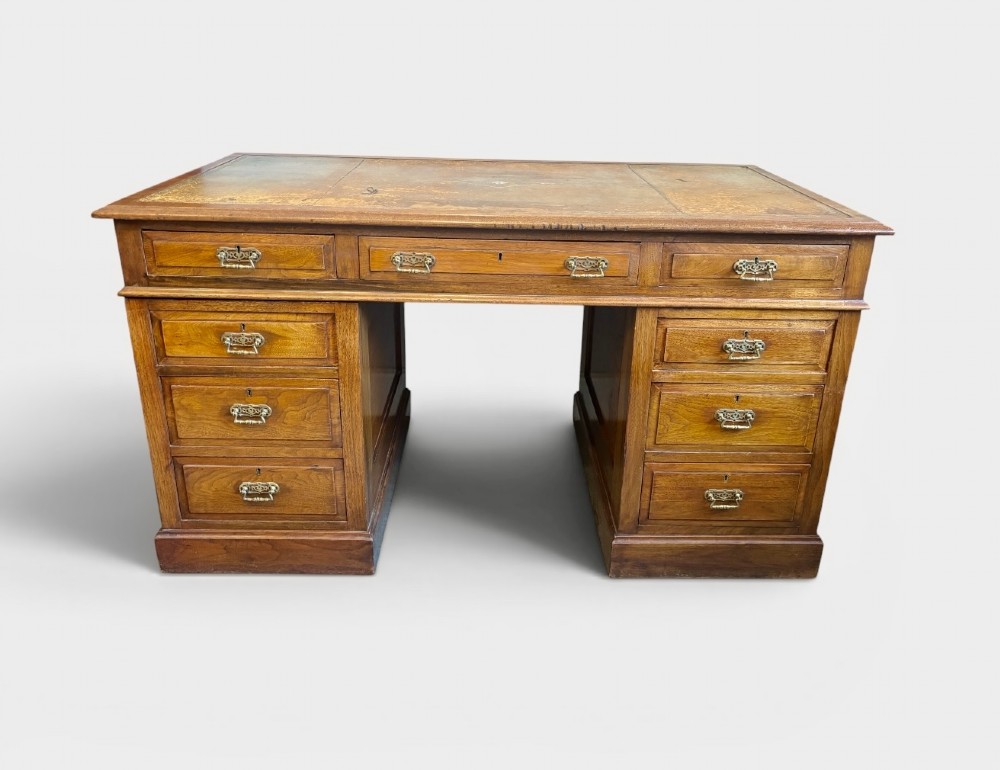 A Victorian walnut pedestal desk featuring nine drawers, brass handles, and a leather insert top surface.