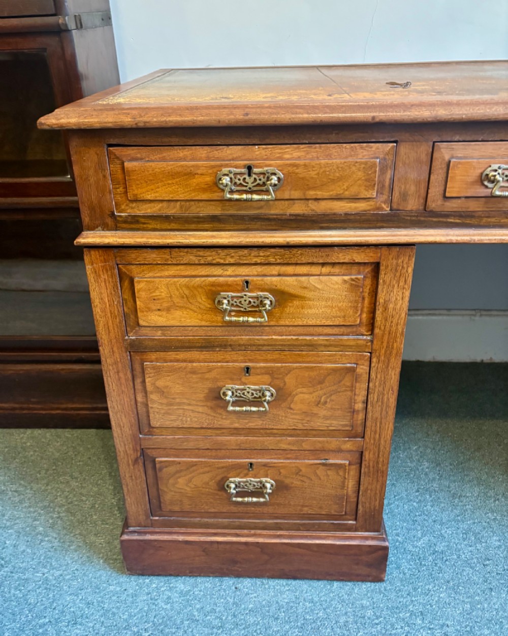 A Victorian walnut pedestal desk featuring nine drawers, brass handles, and a leather insert top surface. View V
