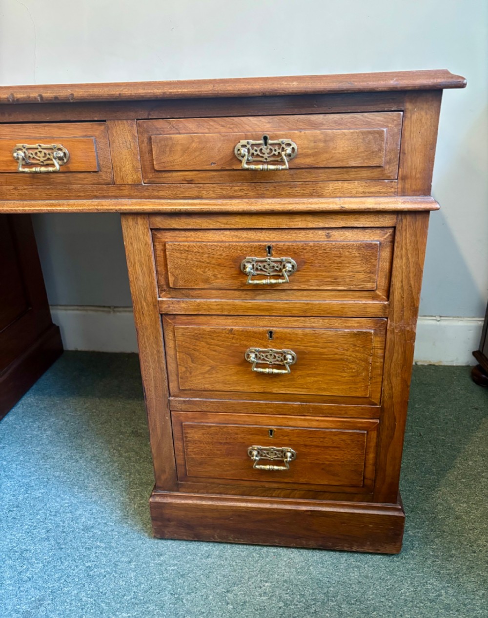 A Victorian walnut pedestal desk featuring nine drawers, brass handles, and a leather insert top surface. View VI