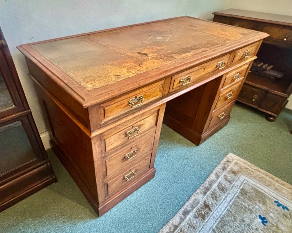 A Victorian walnut pedestal desk featuring nine drawers, brass handles, and a leather insert top surface. View VIII