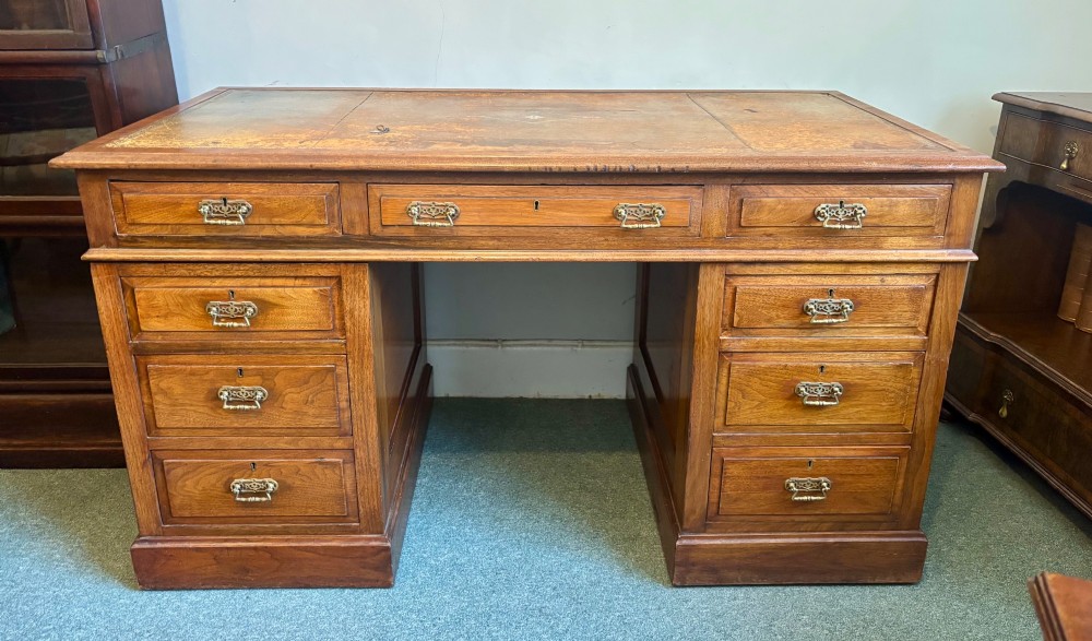 A Victorian walnut pedestal desk featuring nine drawers, brass handles, and a leather insert top surface. View IX