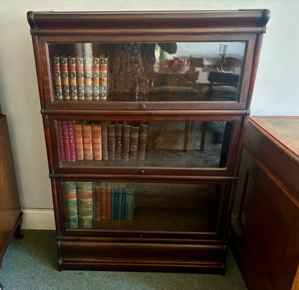 A three-tier Victorian dark oak barrister bookcase featuring glazed lifting doors with small brass knobs. View IV