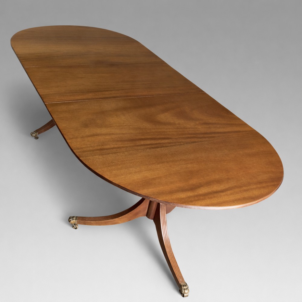 A mahogany twin pillar dining table featuring an oval top with an extension leaf, supported by two splayed pedestal bases with brass castors. View II