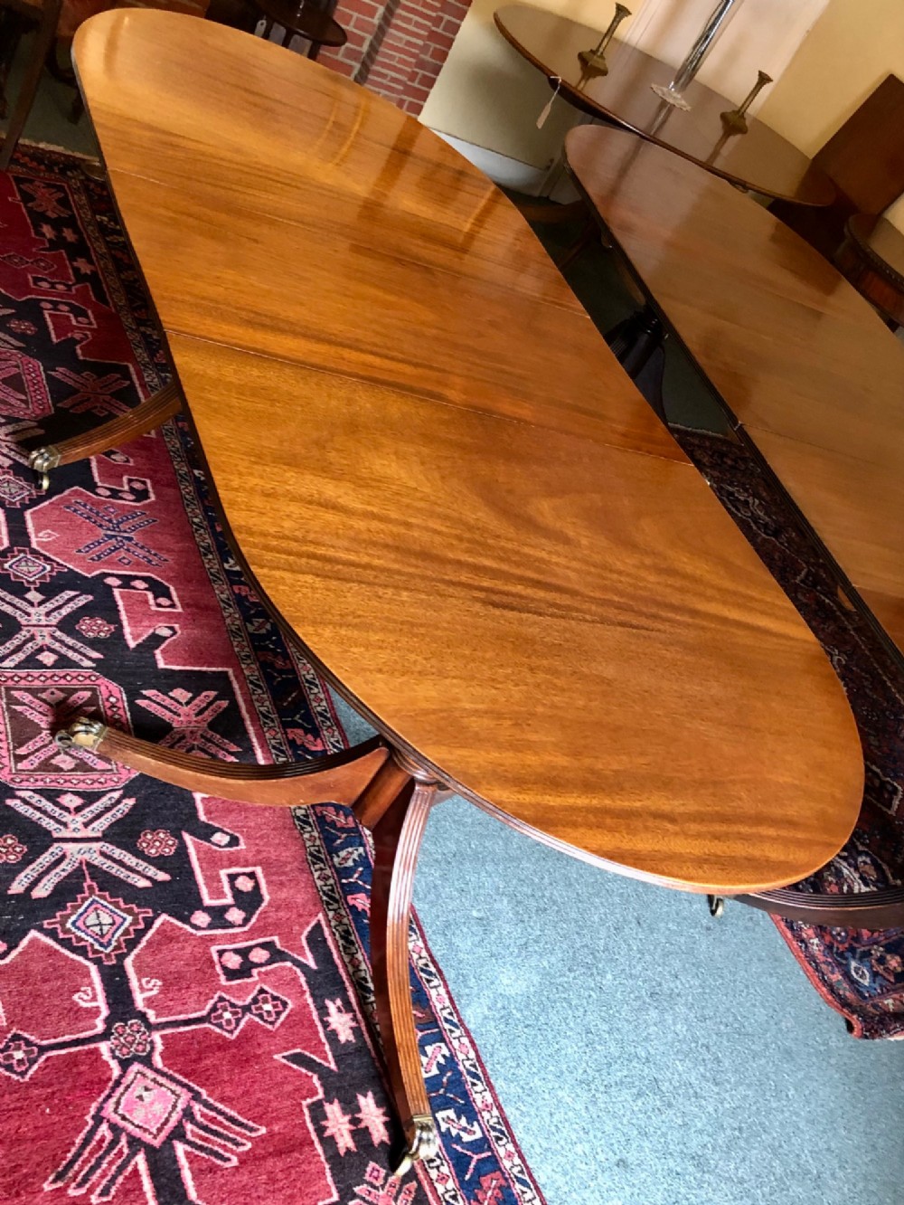 A mahogany twin pillar dining table featuring an oval top with an extension leaf, supported by two splayed pedestal bases with brass castors. View III