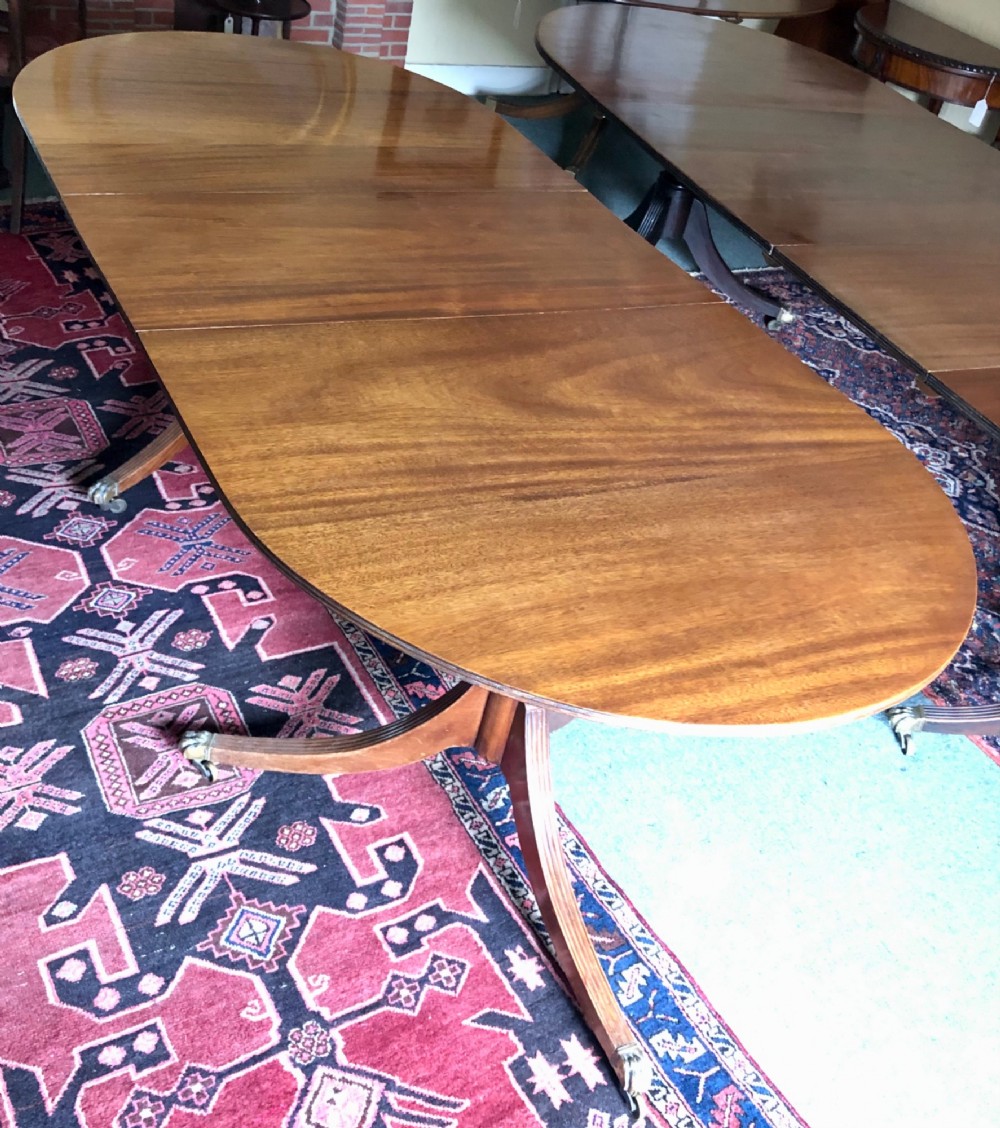 A mahogany twin pillar dining table featuring an oval top with an extension leaf, supported by two splayed pedestal bases with brass castors. View VI