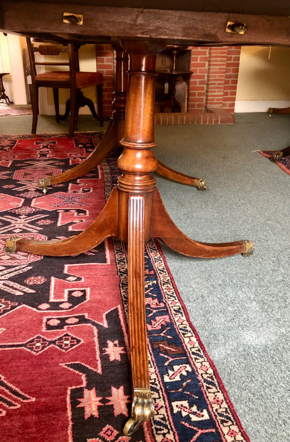 A mahogany twin pillar dining table featuring an oval top with an extension leaf, supported by two splayed pedestal bases with brass castors. View VII