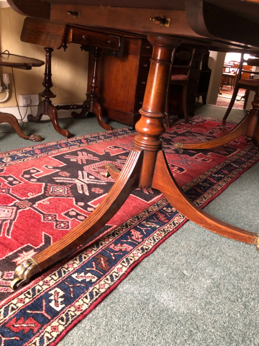A mahogany twin pillar dining table featuring an oval top with an extension leaf, supported by two splayed pedestal bases with brass castors. View IX