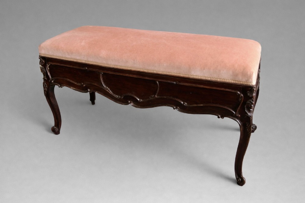 An Edwardian carved rosewood duet stool with a long, dusty-pink velvet upholstered top supported by cabriole legs. View II