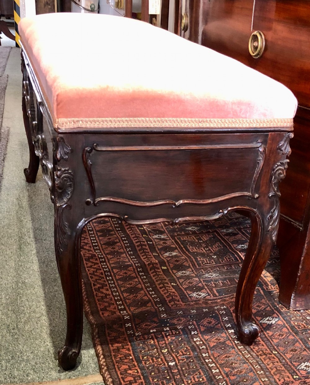 An Edwardian carved rosewood duet stool with a long, dusty-pink velvet upholstered top supported by cabriole legs. View IV