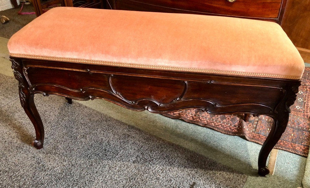 An Edwardian carved rosewood duet stool with a long, dusty-pink velvet upholstered top supported by cabriole legs. View VI