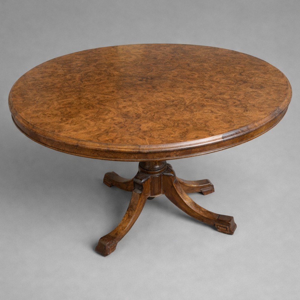 A Victorian oval burr walnut tilt-top table shown angled upright to display the wood veneer pattern and four splayed pedestal legs. View III