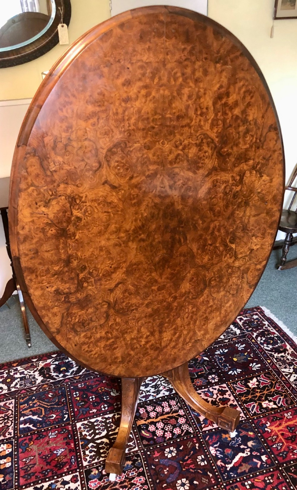A Victorian oval burr walnut tilt-top table shown angled upright to display the wood veneer pattern and four splayed pedestal legs. View V
