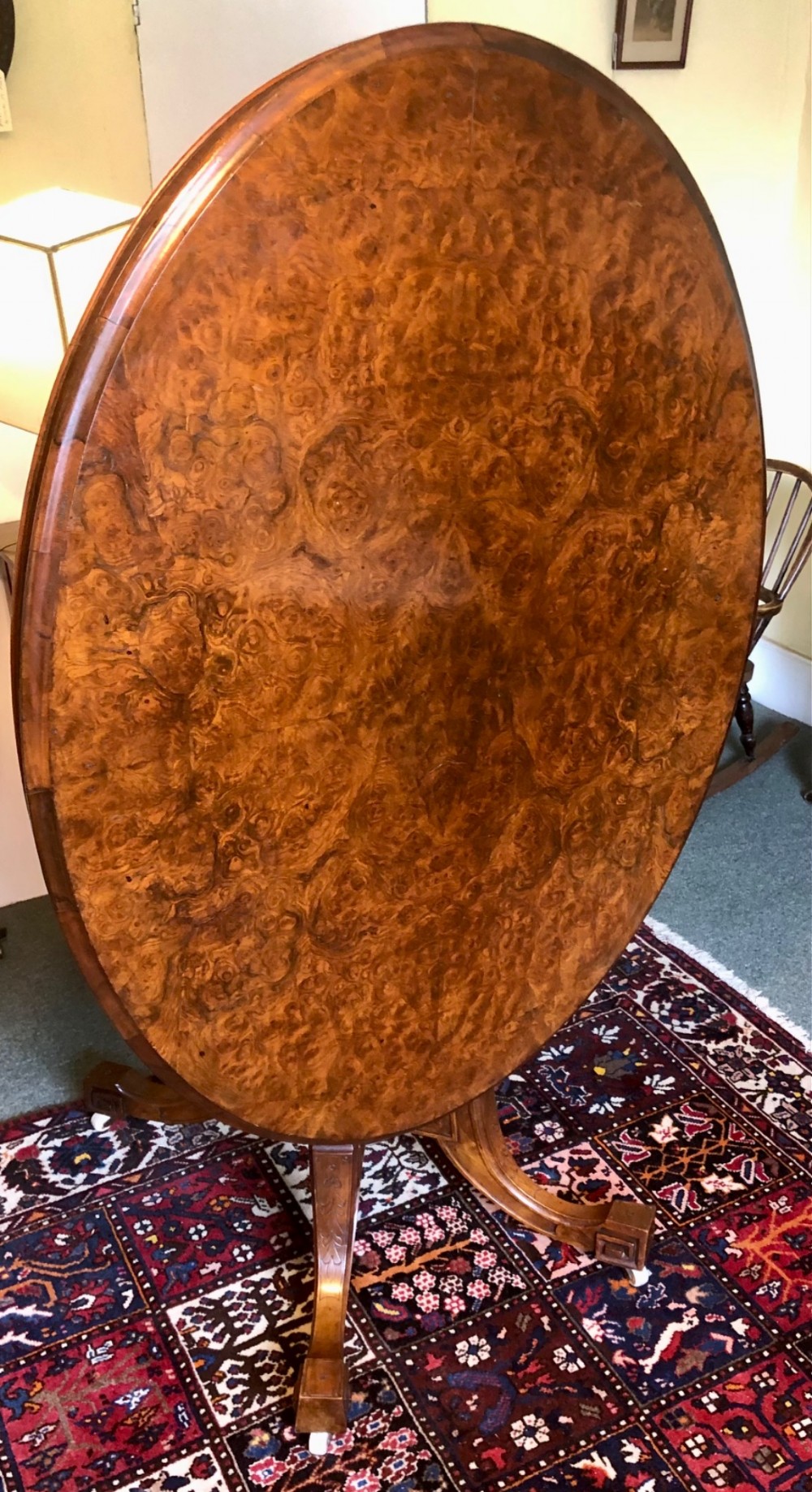 A Victorian oval burr walnut tilt-top table shown angled upright to display the wood veneer pattern and four splayed pedestal legs. View VI