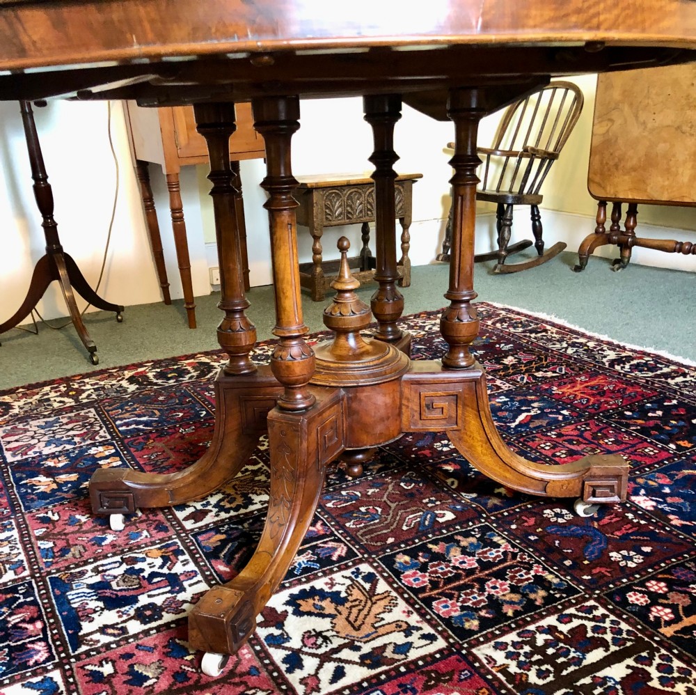 A Victorian oval burr walnut tilt-top table shown angled upright to display the wood veneer pattern and four splayed pedestal legs. View VII