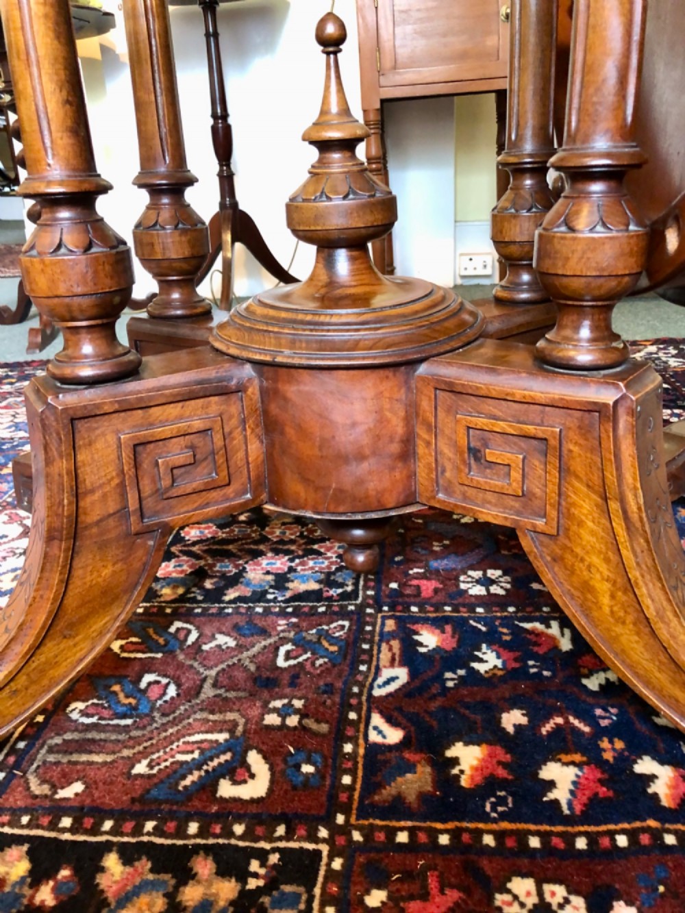 A Victorian oval burr walnut tilt-top table shown angled upright to display the wood veneer pattern and four splayed pedestal legs. View VIII