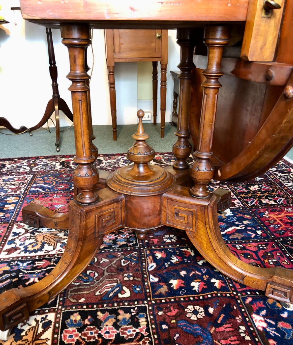 A Victorian oval burr walnut tilt-top table shown angled upright to display the wood veneer pattern and four splayed pedestal legs. View IX