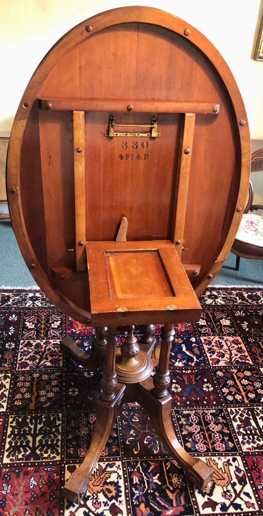 A Victorian oval burr walnut tilt-top table shown angled upright to display the wood veneer pattern and four splayed pedestal legs. View XIII