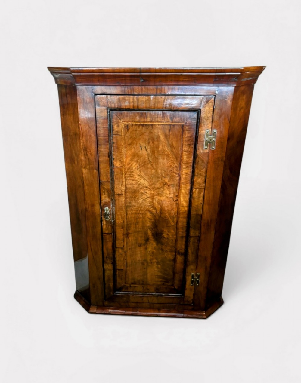A George III walnut corner cupboard featuring a single panelled door with figured wood grain, brass H-hinges, and moulded cornice details.