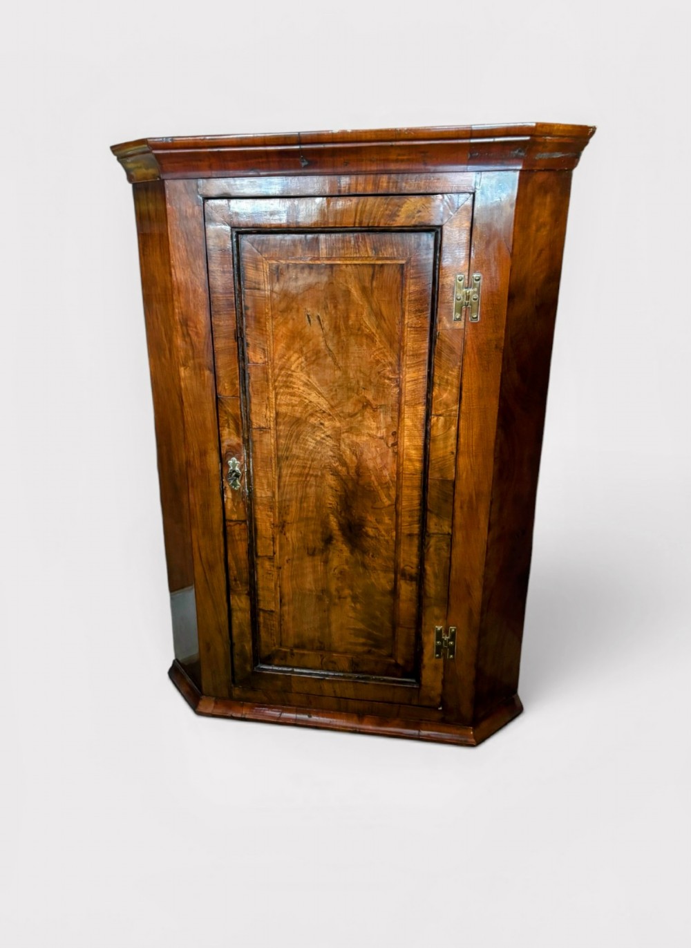 A George III walnut corner cupboard featuring a single panelled door with figured wood grain, brass H-hinges, and moulded cornice details. View II