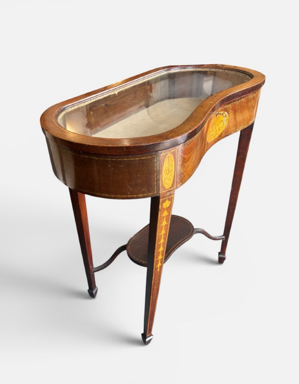 A kidney-shaped Edwardian mahogany display table with satinwood floral inlays, slender tapered legs, a glass top, and an undershelf. View II