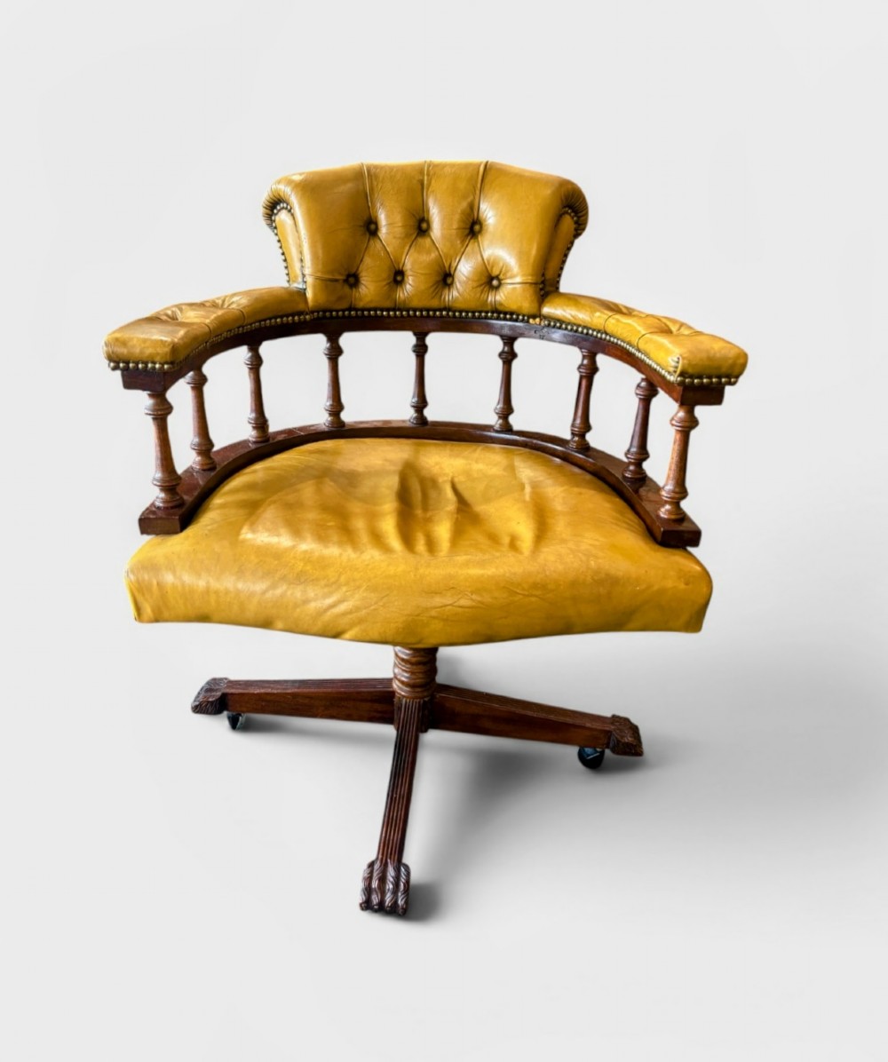 An early twentieth-century mahogany swivel desk chair featuring mustard yellow button-tufted leather upholstery, a horseshoe spindle backrest, and a four-star base with castors.