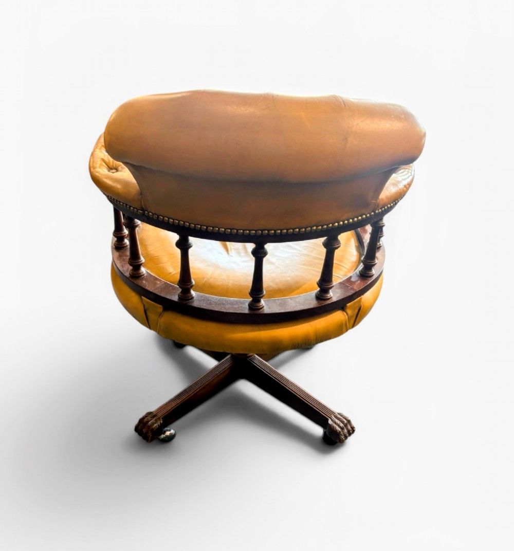 An early twentieth-century mahogany swivel desk chair featuring mustard yellow button-tufted leather upholstery, a horseshoe spindle backrest, and a four-star base with castors. View II