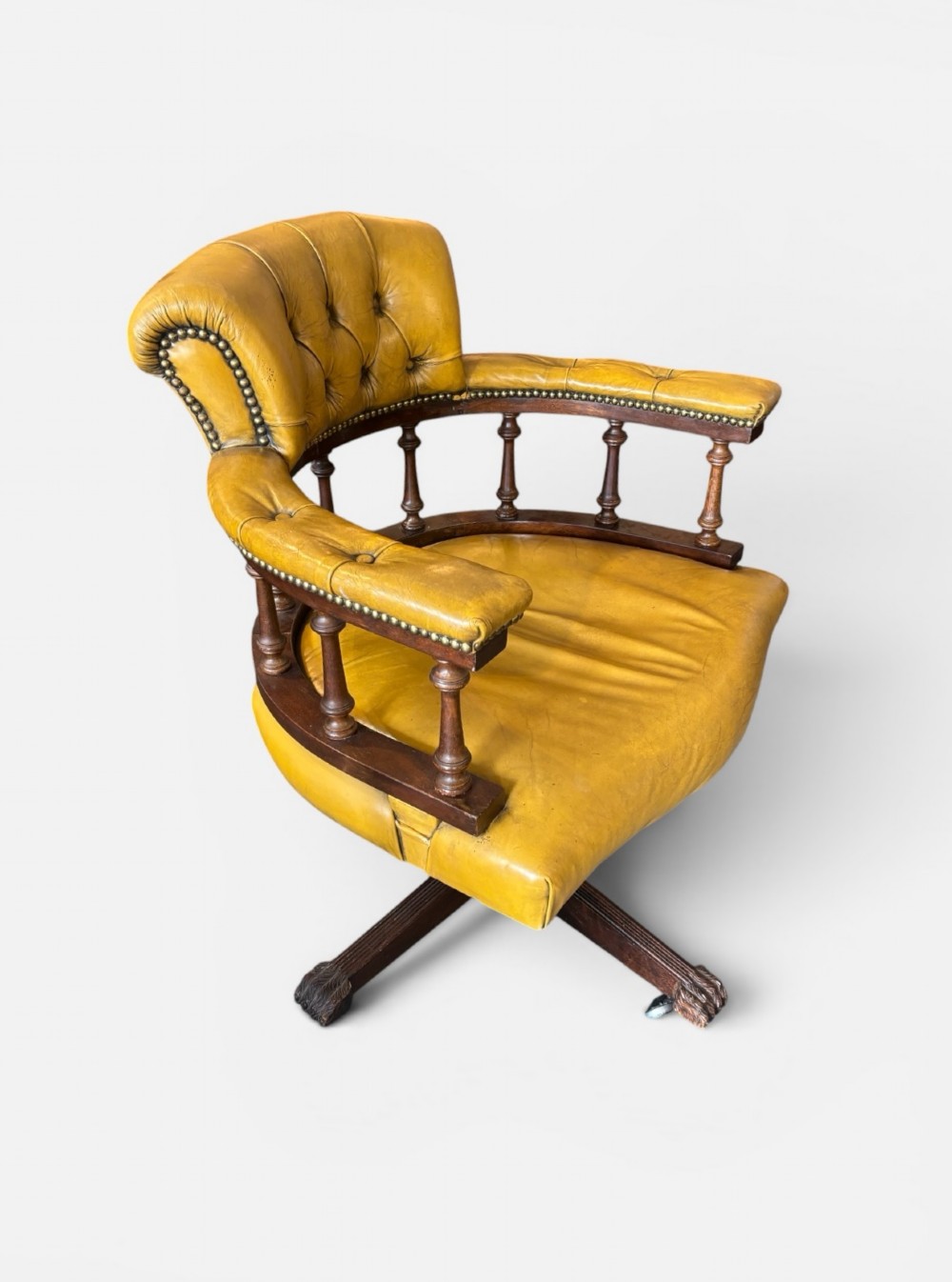 An early twentieth-century mahogany swivel desk chair featuring mustard yellow button-tufted leather upholstery, a horseshoe spindle backrest, and a four-star base with castors. View III