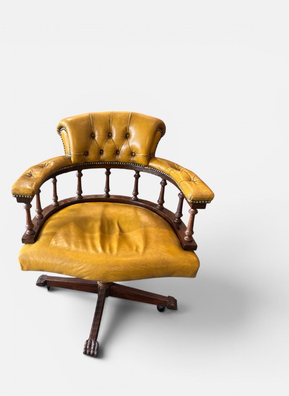 An early twentieth-century mahogany swivel desk chair featuring mustard yellow button-tufted leather upholstery, a horseshoe spindle backrest, and a four-star base with castors. View IV