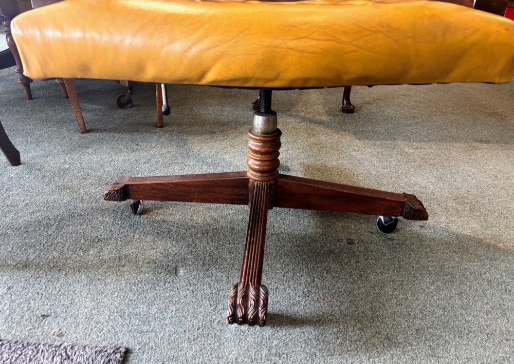 An early twentieth-century mahogany swivel desk chair featuring mustard yellow button-tufted leather upholstery, a horseshoe spindle backrest, and a four-star base with castors. View V