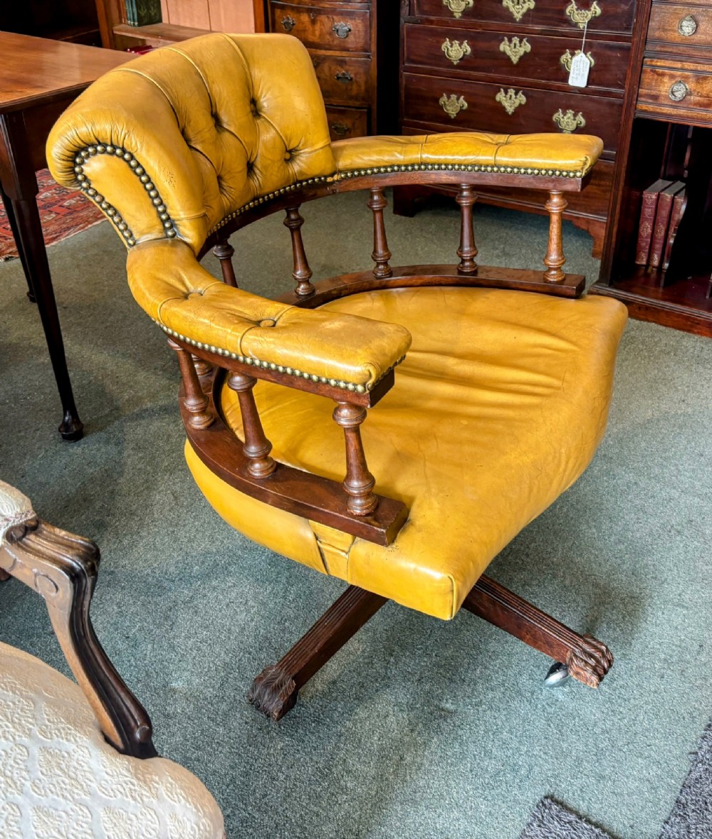 An early twentieth-century mahogany swivel desk chair featuring mustard yellow button-tufted leather upholstery, a horseshoe spindle backrest, and a four-star base with castors. View VI