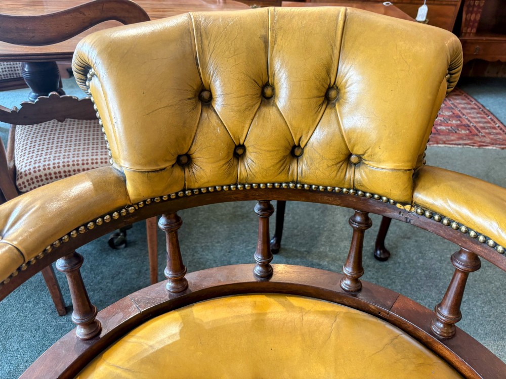 An early twentieth-century mahogany swivel desk chair featuring mustard yellow button-tufted leather upholstery, a horseshoe spindle backrest, and a four-star base with castors. View VII