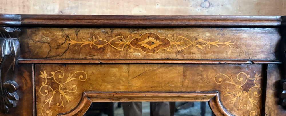 A Victorian walnut side cabinet featuring floral marquetry inlays, three glazed doors, carved corbels, and a shaped serpentine front. View VI