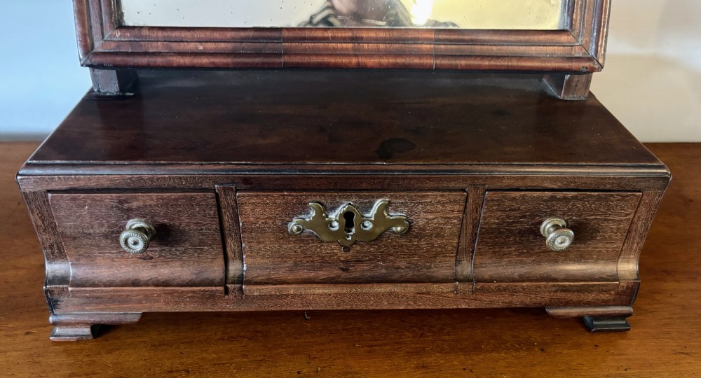 A George III mahogany toilet mirror featuring an adjustable swing plate mounted above a plinth base with three drawers and brass hardware. View IV