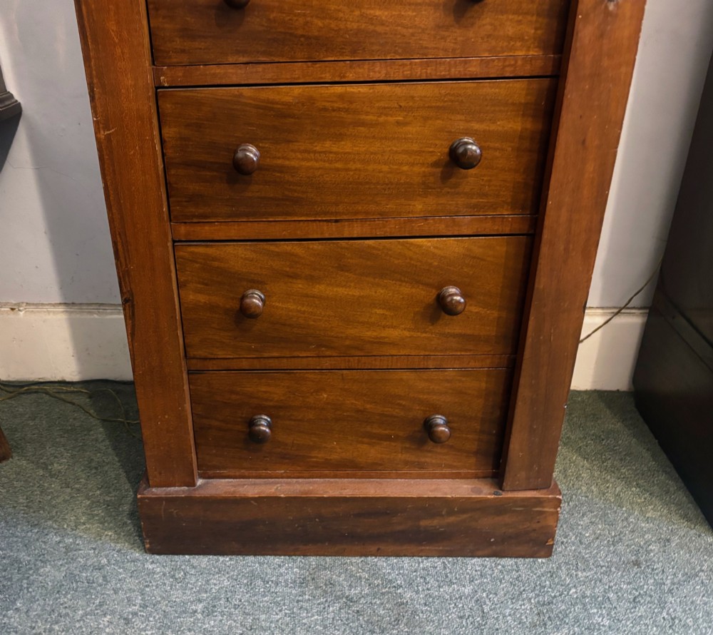 A tall Victorian walnut Wellington chest featuring seven stacked drawers, a right-hand locking stile, carved corner corbels, and turned wooden handles on a plinth base. View VI
