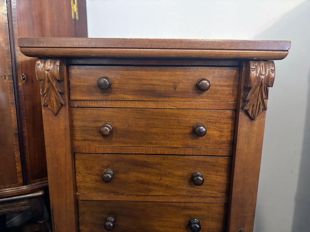 A tall Victorian walnut Wellington chest featuring seven stacked drawers, a right-hand locking stile, carved corner corbels, and turned wooden handles on a plinth base. View VIII