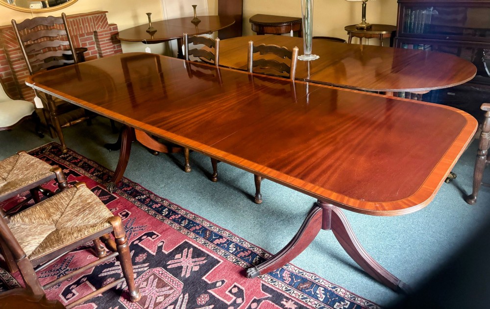 A Regency style mahogany twin pillar dining table featuring a crossbanded top and splayed quadruped feet on brass castors.