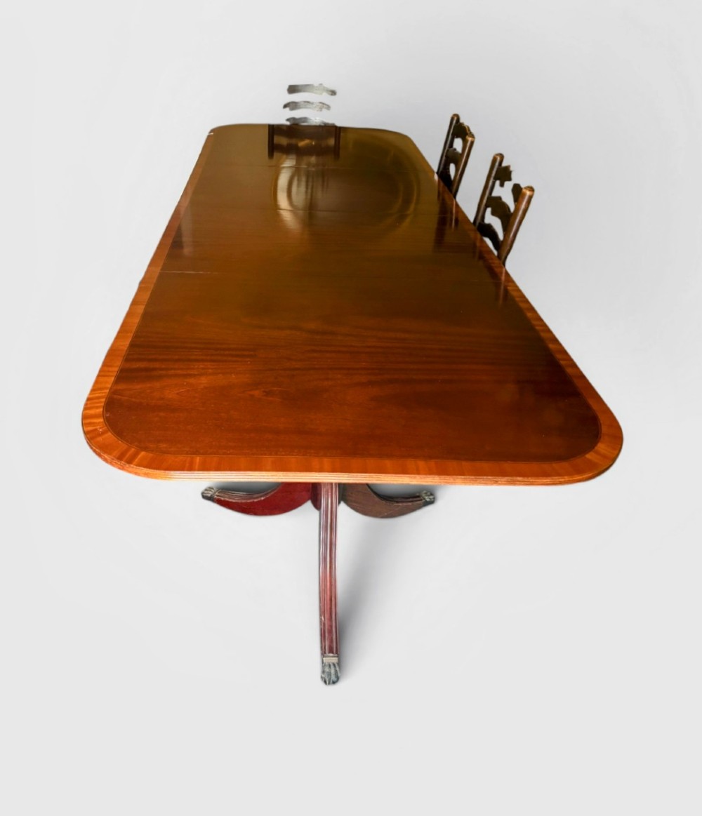 A Regency style mahogany twin pillar dining table featuring a crossbanded top and splayed quadruped feet on brass castors. View II