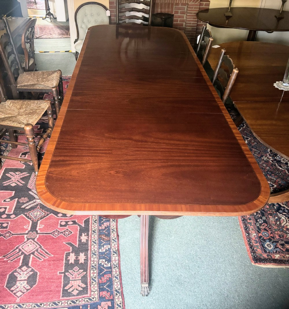 A Regency style mahogany twin pillar dining table featuring a crossbanded top and splayed quadruped feet on brass castors. View IV