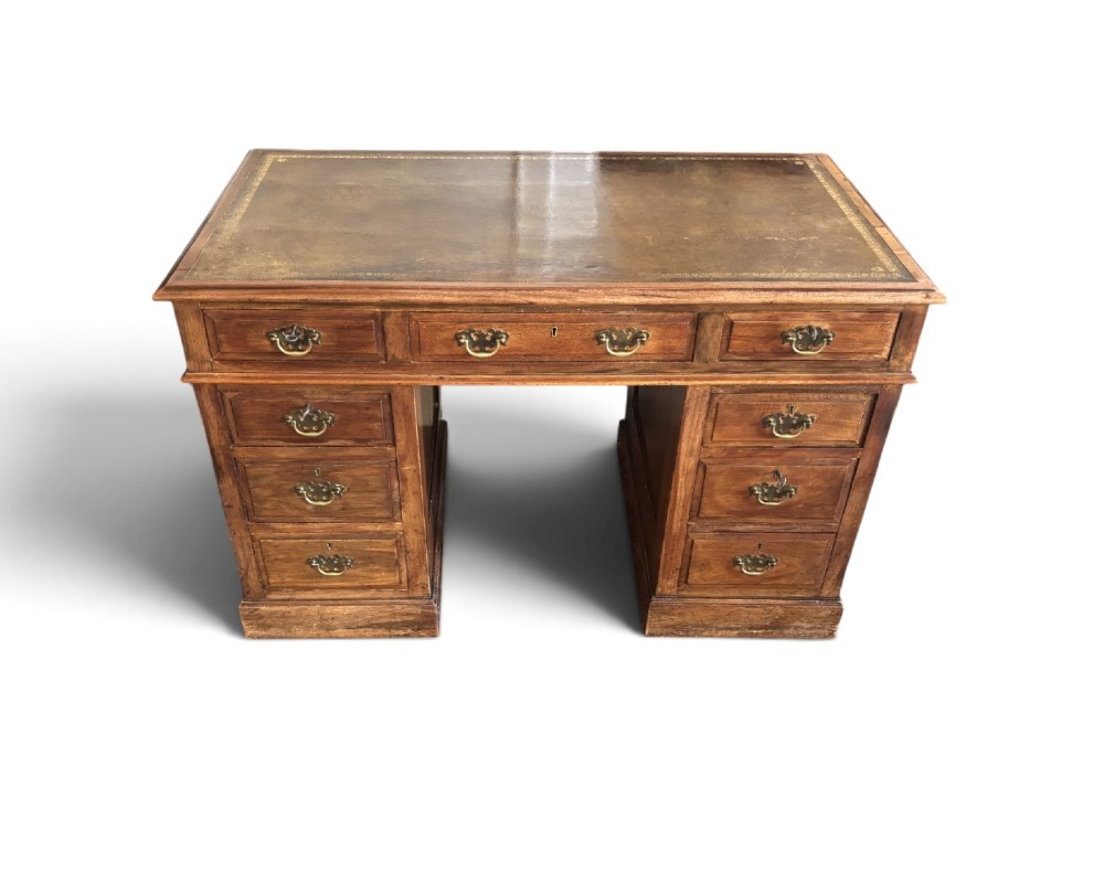 A Victorian walnut pedestal desk featuring nine drawers with brass handles and a gilt-tooled leather writing top.