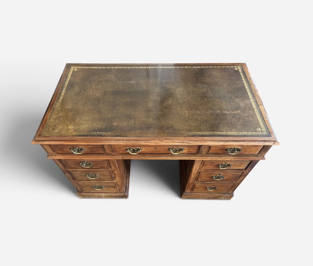 A Victorian walnut pedestal desk featuring nine drawers with brass handles and a gilt-tooled leather writing top. View VI