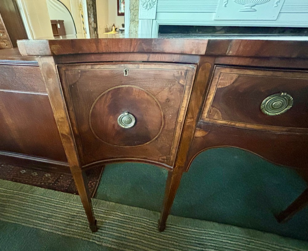 A George III mahogany serpentine-front sideboard featuring circular inlaid drawer details, brass ring handles, and square tapered legs. View III