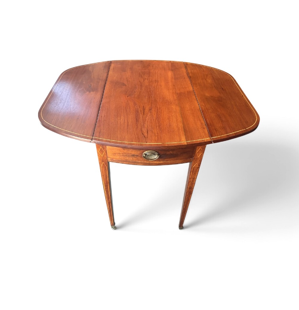A Regency mahogany oval supper table with twin drop leaves, fine boxwood inlay, a central frieze drawer, and square tapered legs on brass castors. View II