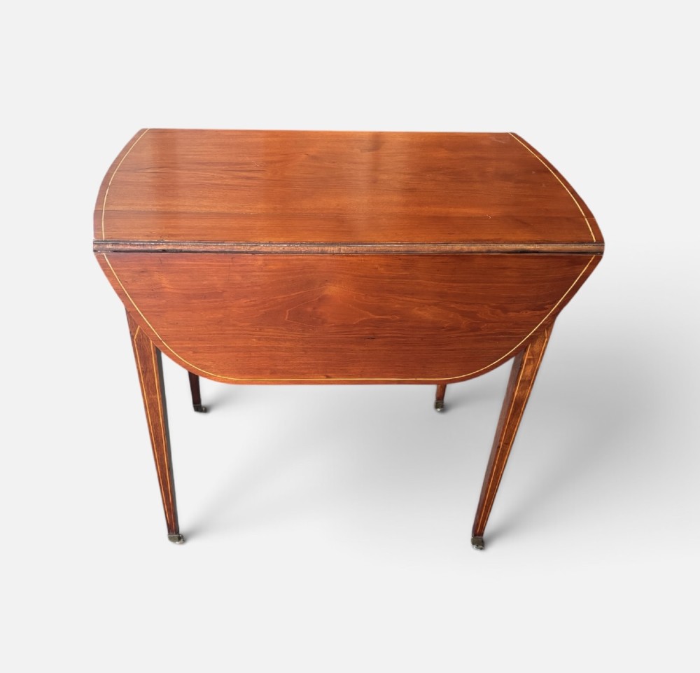 A Regency mahogany oval supper table with twin drop leaves, fine boxwood inlay, a central frieze drawer, and square tapered legs on brass castors. View V