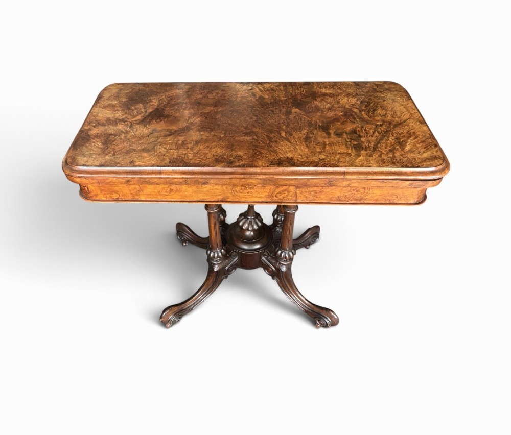 A Victorian rectangular flip-top card table made from figured walnut wood, featuring rounded corners and a carved quad-form pedestal base.