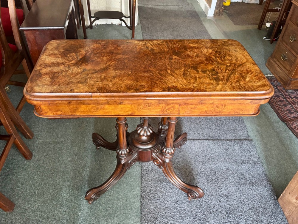 A Victorian rectangular flip-top card table made from figured walnut wood, featuring rounded corners and a carved quad-form pedestal base. View VI