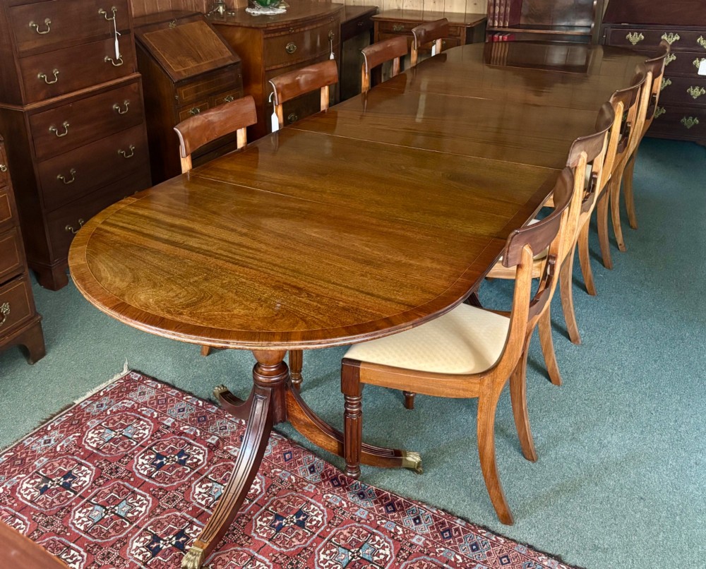 A large polished Regency design mahogany dining table featuring a triple pedestal base with inlaid edge details and brass castors. View II