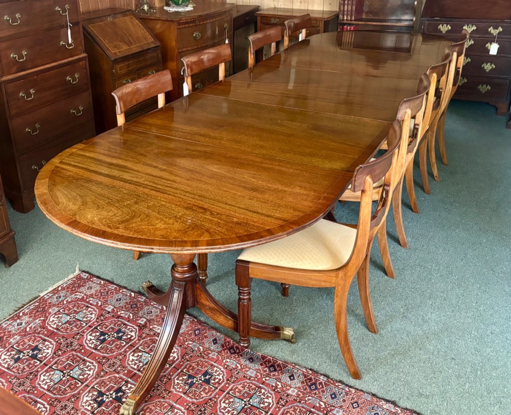 A large polished Regency design mahogany dining table featuring a triple pedestal base with inlaid edge details and brass castors. View III