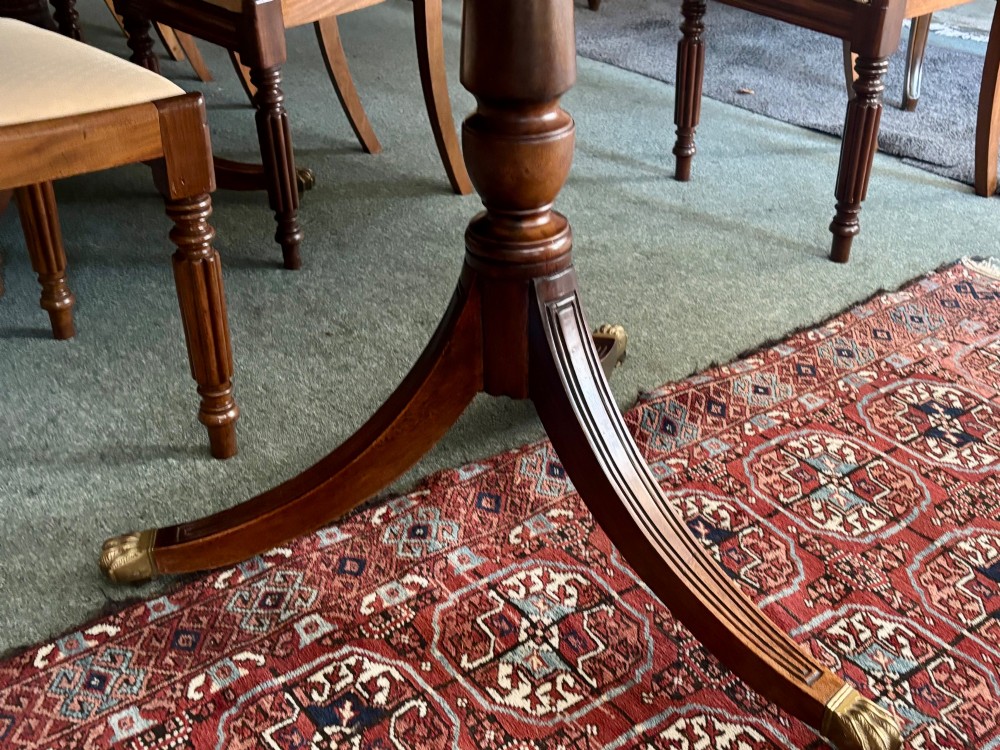 A large polished Regency design mahogany dining table featuring a triple pedestal base with inlaid edge details and brass castors. View IV