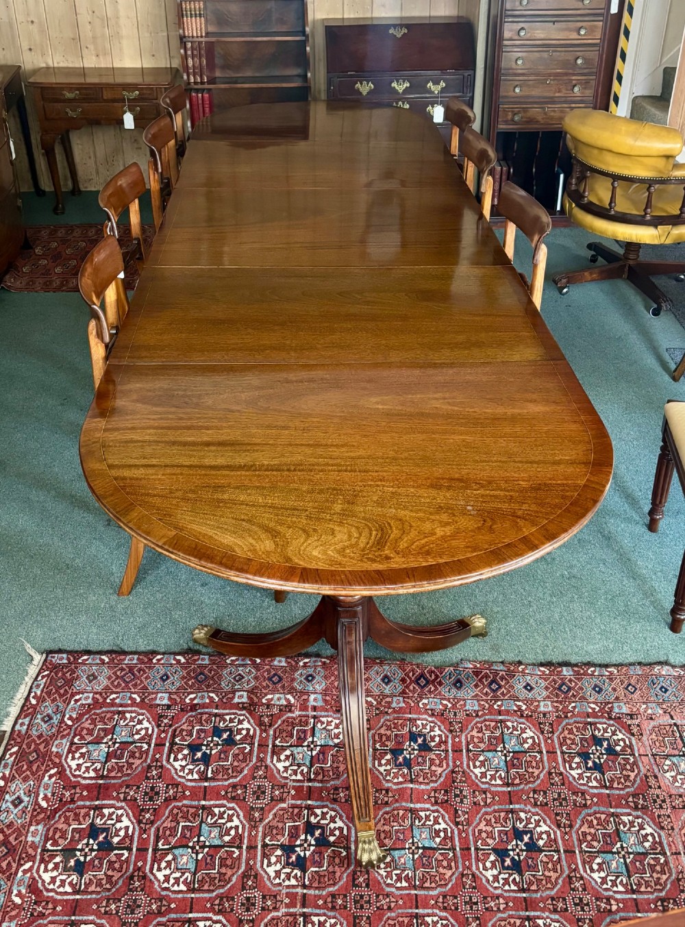 A large polished Regency design mahogany dining table featuring a triple pedestal base with inlaid edge details and brass castors. View V