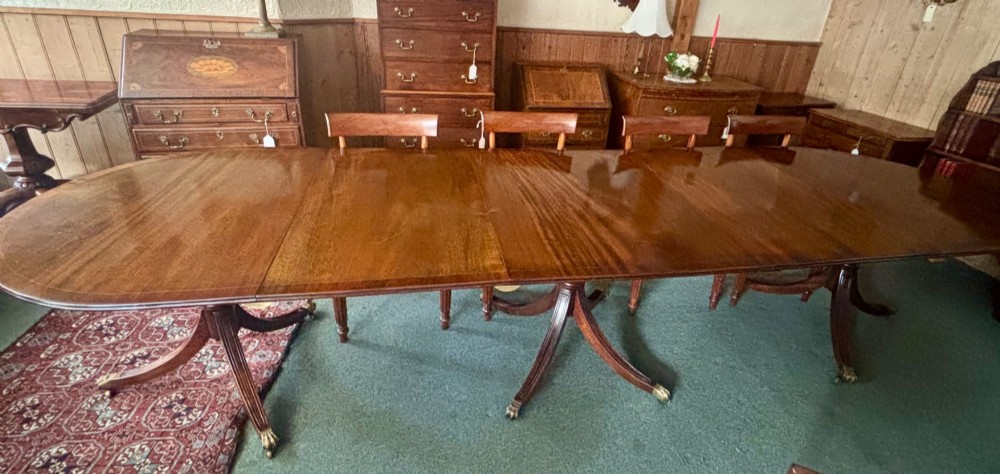 A large polished Regency design mahogany dining table featuring a triple pedestal base with inlaid edge details and brass castors. View VI